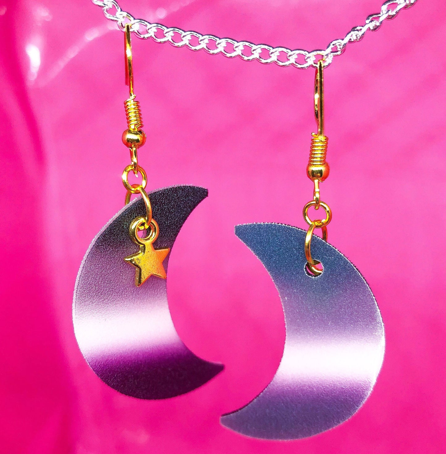 Shrinky dink earrings in the shape of a crescent moon. The colour of the charm is the asexual pride flag with a small gold star charm hanging at the top.