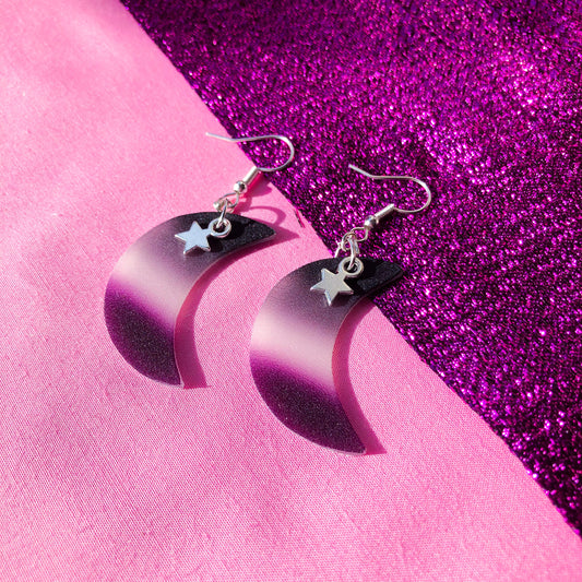 Shrinky dink earrings in the shape of a crescent moon. The colour of the charm is the asexual pride flag with a small gold star charm hanging at the top.